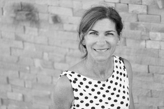 Ritratto di donna cinquantenne bianca con canotta a pois che sorride su uno sfondo di mattoni in pietra