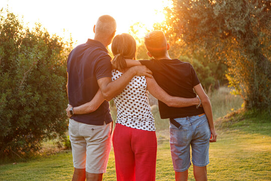 Famiglia composta da tre persone , di spalle ,si abbraccia in segno di unione rivolti verso il tramonto in un contesto naturale