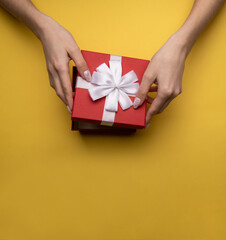 Flat lay of woman hands holding present with red box decorated with white ribbon