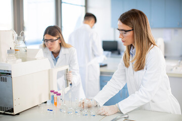 Female scientists in a white lab coat putting vial with a sample for an analysis on a...