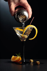 Dry martini with lemon peel and green olives on a black background.