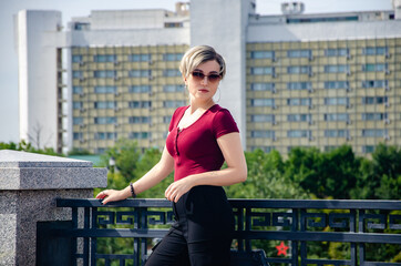 A girl with glasses stands next to a metal fence against the background of buildings