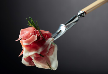 Sliced prosciutto with rosemary on a fork.
