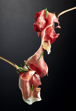 Sliced prosciutto with rosemary on forks.