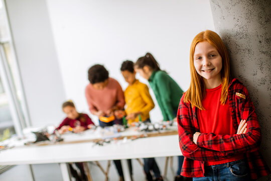 Cute little girl standing in front of kids programming electric toys and robots at robotics classroom
