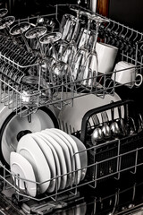 Clean dishes in the dishwasher. Wine glasses, glasses, cups, plates, cutlery. Close-up. Washing-up and housework concept. Vertical shot