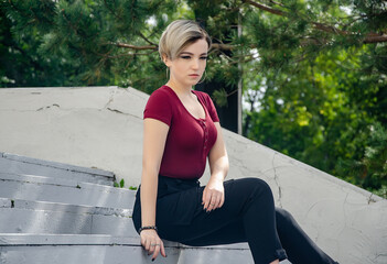 The girl is sitting on a concrete ladder against the background of trees