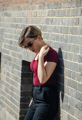 Close up of a girl in glasses and a red jacket standing against a brick wall