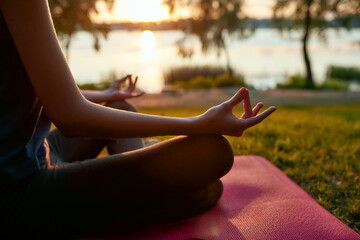 Cropped shot of a woman practicing yoga in the morning outdoors, sitting in lotus pose and meditating on the background of nature