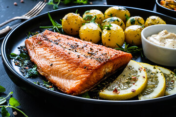 Fried salmon fillet with boiled potatoes, vegetable salad, lemon and mayonnaise served on black...