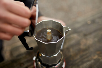 Traveler man making camping coffee outdoor with metal geyser coffee maker on a gas burner, step by...
