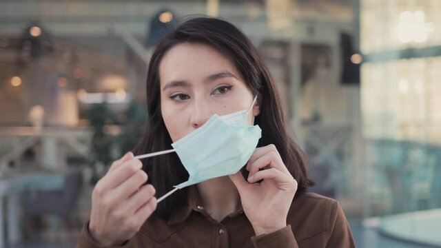 Young woman, portrait shot, put on protective mask, indoors on background of blurred glass windows. Girl in brown shirt in medical protective mask portrait, in the business city mall