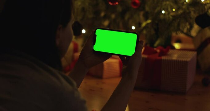 Close up shot of woman lie on floor, texting, typing, chatting on phone next to christmas present, smiling in living room. Christmas time. iPhone 12 green screen.