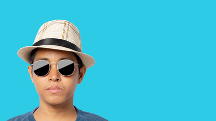 Young man wearing sunglasses and straw hat isolated on a blue background.