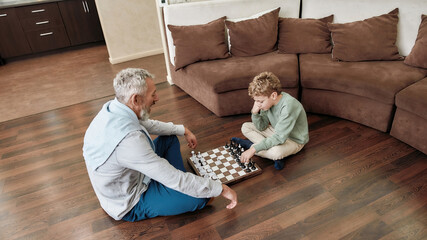 Grandpa teaching his grandson best chess strategy and tactics while sitting together on the floor...
