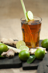 large glass of tea with whole lime and sliced ​​with lemongrass, ginger and lime leaves on a wooden cutting board