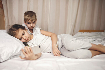 Two siblings watching video in their mobile electronic device in the bed, gadget dependence and addiction, online and internet for the whole day, family lifestyle, indoor
