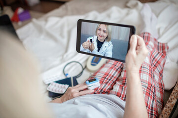 Old woman in bed looking at screen of laptop and consulting with a doctor online at home, telehealth services during lockdown, distant video call, modern tech healthcare application