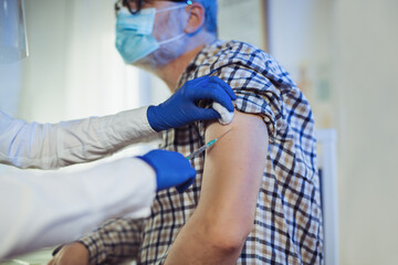 Young woman nurse with surgical mask and face shild giving injection to senior man.