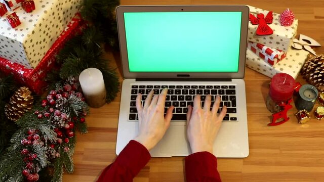 Girl hands typing on laptop keyboard with blank green screen on Christmas background. Chroma key monitor. Free content. Mockup monitor. Online greeting. Internet surfing. New Year Celebrating concept.