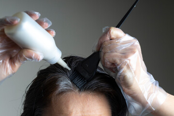 Closeup woman hands dyeing hair using black brush. Middle age woman colouring dark hair with gray...