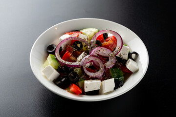 Greek salad with feta cheese and onion rings on top, close view, studio shot on dark background