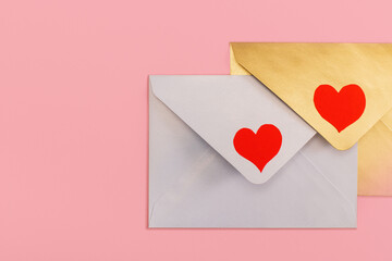light mother-of-pearl and golden paper envelopes with red hearts isolated on pink background