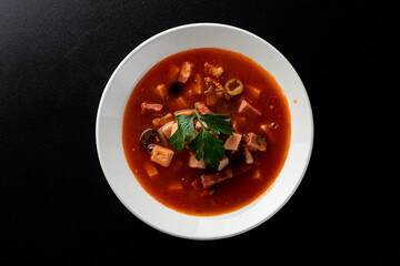 Hot gourmet meat soup solyanka with black olives and tomato broth, bright red on black