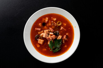 Hot gourmet meat soup solyanka with black olives and tomato broth, bright red on black