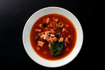 Hot gourmet meat soup solyanka with black olives and tomato broth, bright red on black