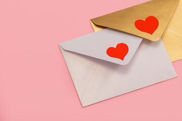 light mother-of-pearl and golden paper envelopes with red hearts isolated on pink background