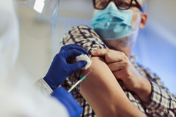 Portrait of bearded old man receiving vaccine shot in hand while wearing face protective mask during covid-19 pandemic. Medicine, vaccination and healthcare concept