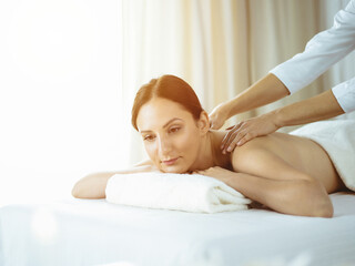 Obraz na płótnie Canvas Pretty brunette woman enjoying procedure of back massage in sunny spa salon. Beauty concept. Cold toned picture