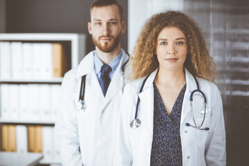 Fototapeta premium Red-bearded doctor with female colleague discussing current disease therapy while sitting at working place in clinic. Team work in medicine