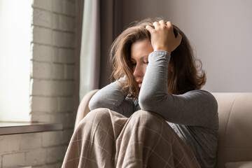 Sad scared woman in panic attack grabbing her head by hand. Lonely girl wrapped in a plaid sitting...