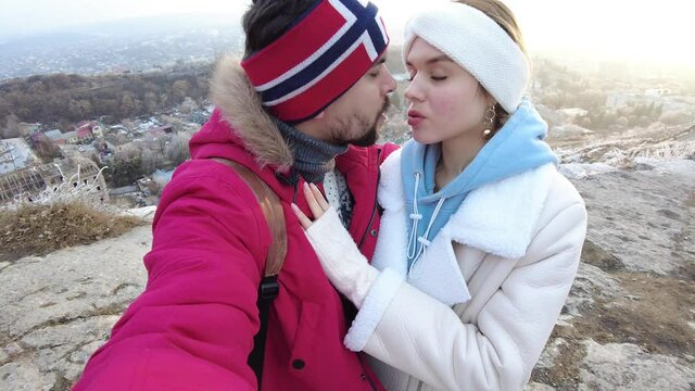 A guy and a girl stand on the edge of a rock in an embrace in winter and kiss, joy appears on their faces