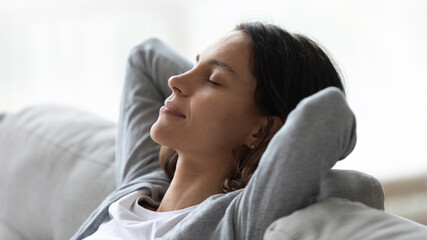 Close up peaceful woman with closed eyes resting on couch at home, leaning back, sitting with hands...
