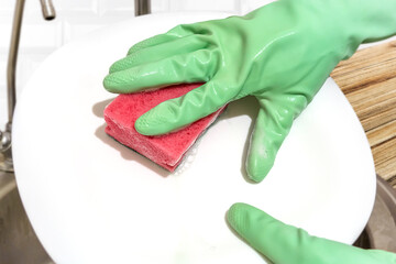 Hands in green protective glove washing dishes