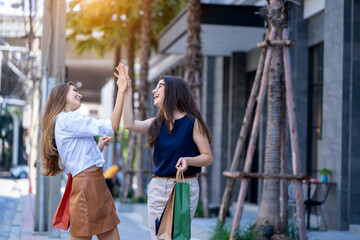 Two young attractive girls with shopping bags after shopping in the mall and smiling while walking down the street.