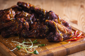 appetizing, golden chicken wings baked on the grill served on a wooden board, background with elements of fresh greens, top view. Dark background, low key