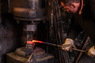 Real brutal blacksmith works in a workshop mechanical hammer with a red-hot iron. Portrait of a profession.