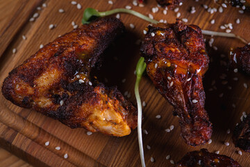 appetizing, golden chicken wings baked on the grill served on a wooden board, background with elements of fresh greens, top view. Dark background, low key