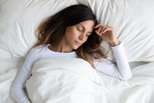 Top View From Above Peaceful Beautiful Young Woman Sleeping In Bed On Comfortable Soft Pillow, Attractive Female Resting With Closed Eyes, Lying Under Warm Blanket, Enjoying Fresh Bedclothes