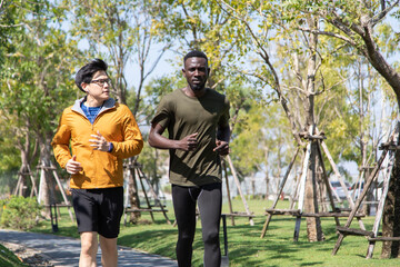 Two sport people black man and asian man jogging and running together in park at autumn morning.
