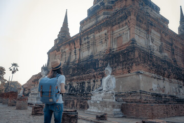 Asian woman tourists carrying a backpack and wearing a hat Visit Wat Yai Chaimongkol, the historical archaeological site of Phra Nakhon, Ayutthaya.