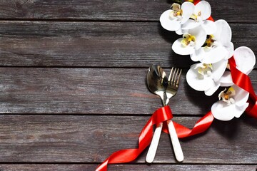 Cutlery, orchid flower and red ribbon on a wooden background. Festive dinner for Valentine's Day.