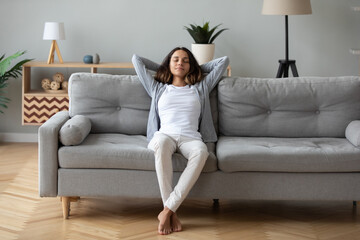 Obraz premium Full length peaceful woman with closed eyes resting on couch, leaning back with hands behind head, enjoying lazy weekend at home, calm young female relaxing, daydreaming, taking nap on sofa