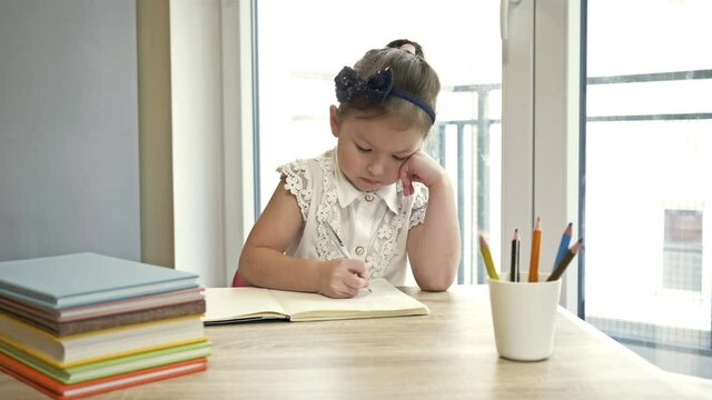 Little elementary schoolgirl doing homework. Cute child learns on his own. Back to school.