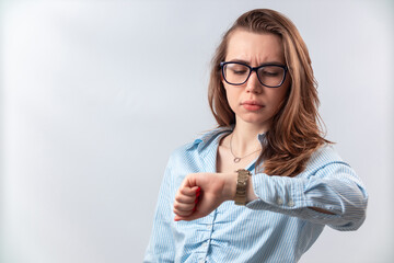 beautiful girl in a blue shirt and glasses looks at the clock on a white background. isolated - obrazy, fototapety, plakaty