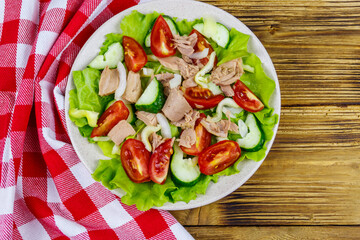 Tasty tuna salad with lettuce and fresh vegetables on wooden table. Top view